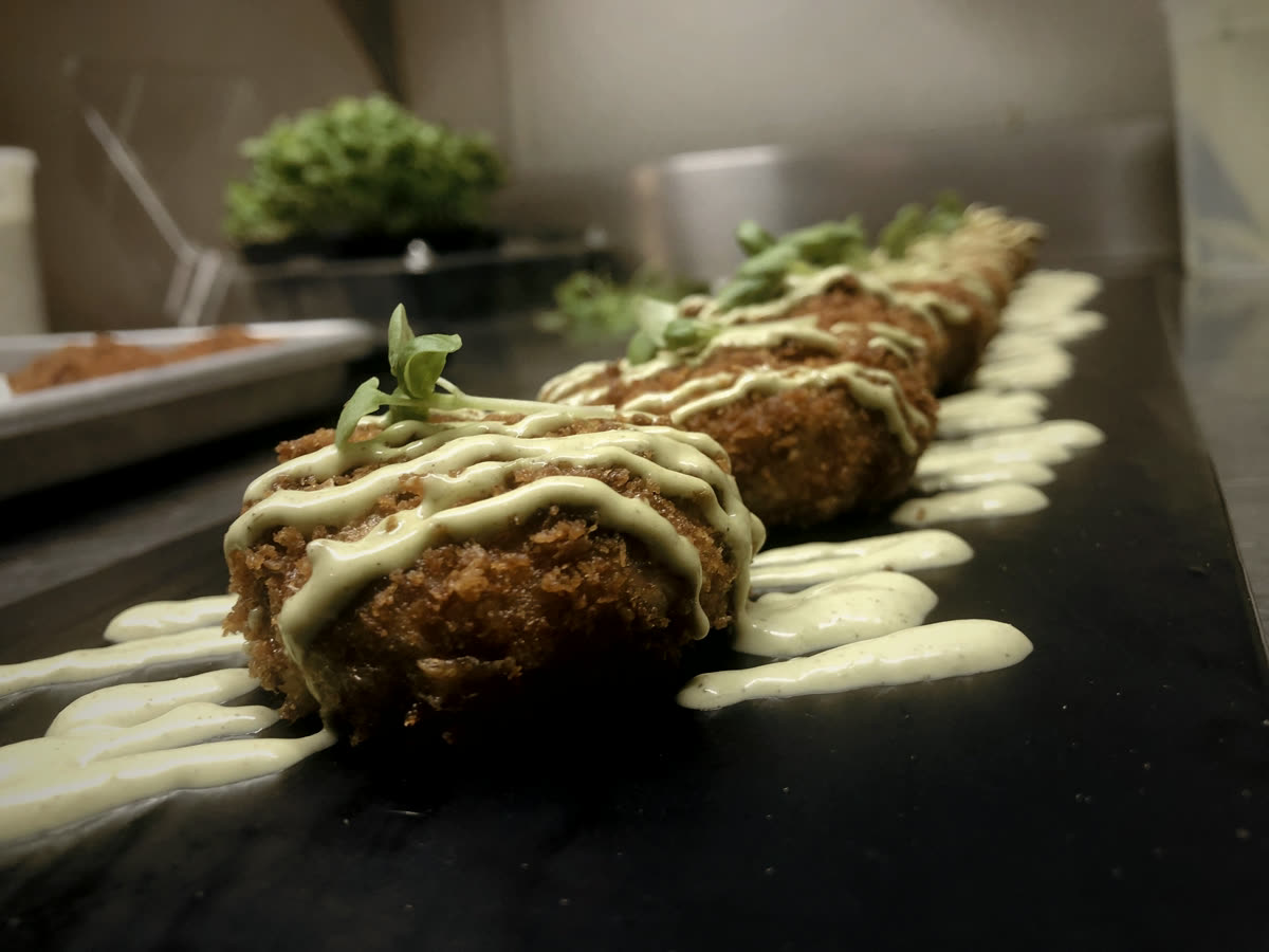 Panko-crusted seafood croquettes drizzled with herb aioli, plated live on dark slate