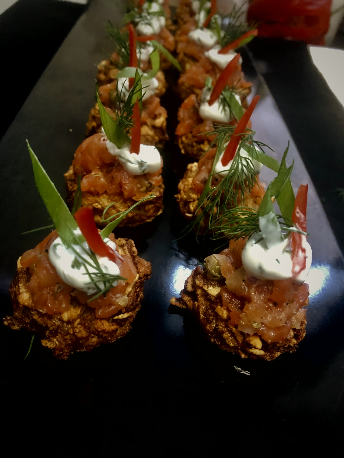 A row of fresh salmon tartare canapés with dill and crème fraîche on dark slate