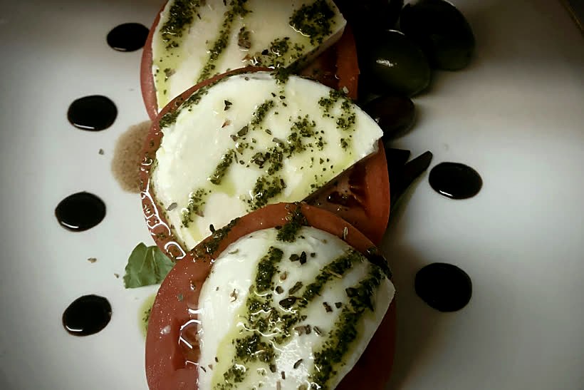 A restrained caprese of sliced tomato, fresh mozzarella and basil oil, quietly plated