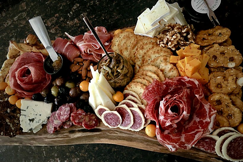 An abundant charcuterie board with cured meats, artisan cheeses, crackers and fruit on live-edge wood