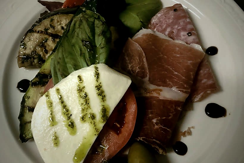 An antipasto plate of prosciutto, fresh mozzarella caprese, grilled vegetables and olives
