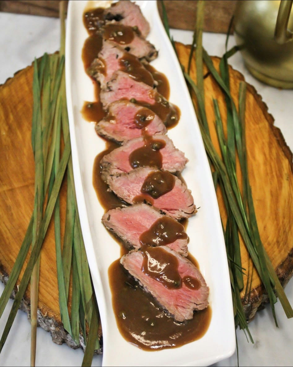 Sliced herb-crusted beef tenderloin with red wine demi-glace, served on a long white platter